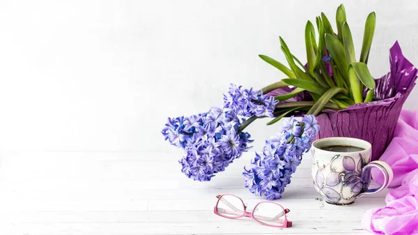 A still life of purple Hyacinth flower blooms with a cup of coffee in front and copy space to the left.