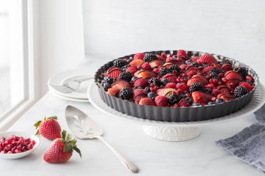 Parlak bir pencereye karşı servis için hazır karışık dutlu cheesecake turtasını kapat..