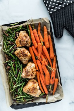 Fırından yeni çıkmış, kızarmış tavuk budu ve sebzelerle dolu bir tavanın tepsi aşağı manzarası..