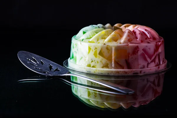黒を背景にガラスのテーブルに反射する虹色のゼリー型デザート — ストック写真