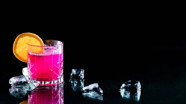 stock image A bright glowing dragonfruit cocktail garnished with an orange slice against a black background. 