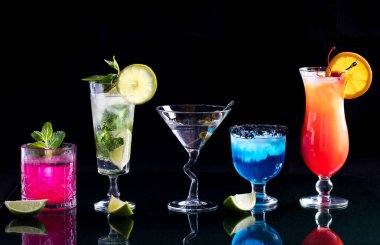 A row of bright colourful cocktails on a glass table, against a black background. clipart