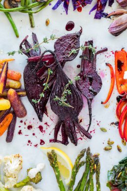 Üzerinde kekik olan ve etrafını çevreleyen diğer sebzelerle birlikte parşömen kağıdının üzerindeki kavrulmuş pancarın en üstten görünüşü.. 