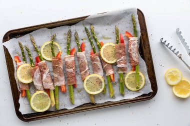 Prosciutto sarılı kuşkonmazla dolu, fırına atılmaya hazır bir çarşafın en alt görüntüsü.. 