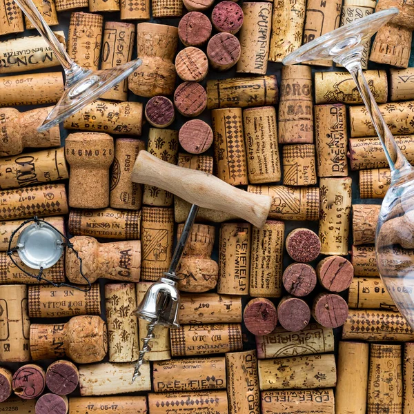 Wine corks in a pattern with wine glasses and corkscrew laying on top. Square crop.