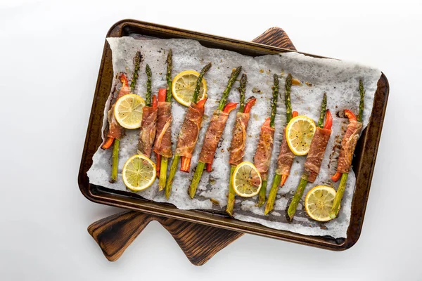 A sheet pan topped with prosciutto wrapped asparagus appetizers on a wooden board.
