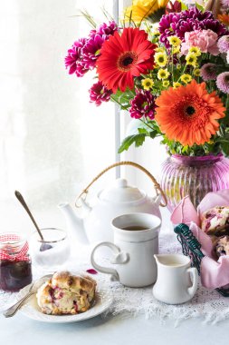 Parlak, güneşli bir pencereye karşı çay, çörek ve renkli çiçekler.. 
