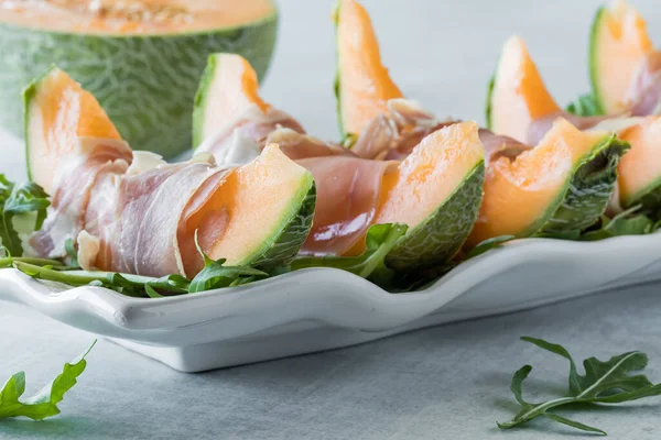 stock image A platter of cantaloupe wedges wrapped in prosciutto deli meat, ready for eating. 