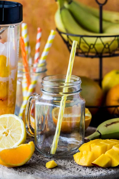 stock image An empty glass jar mug with a straw surrounded by ingredients to make a mango citrus smoothie. 