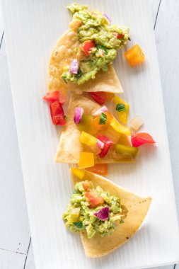 Ev yapımı salsa ve guacamole sosuyla kaplı küçük bir tabakta üç çıtır tortilla cipsi..
