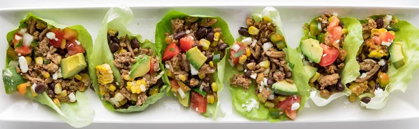A row of healthy ground turkey taco lettuce wraps on a white platter.