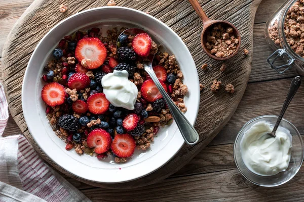 İçinde böğürtlen, granola ve Yunan yoğurdu olan sağlıklı bir kahvaltı kasesinin üstünde..