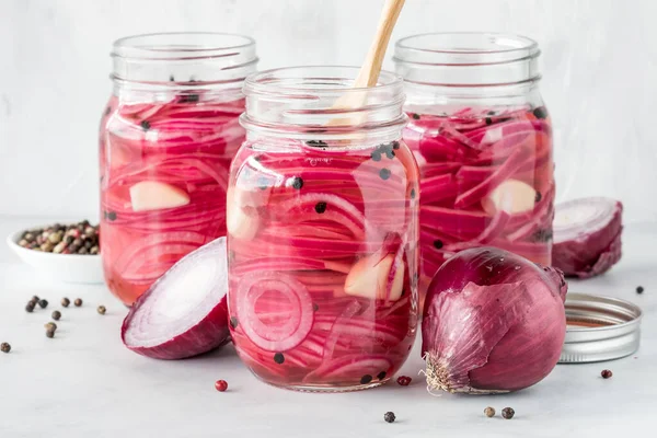 stock image Jars of freshly prepared pickled red onions with peppercorns, against a light background.