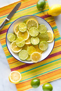 Renkli bir hasırın üzerinde bir tabak taze limon ve limon dilimi..