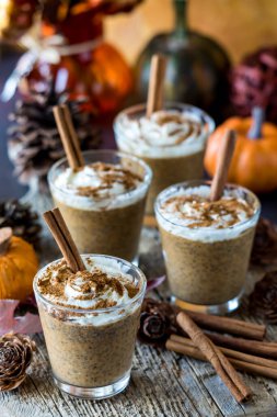 Tarçın çubuklarıyla süslenmiş ve dekorasyonlarla çevrili balkabağı baharatlı chia latte pudingleri..