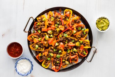 Fırından yeni çıkmış, salsa soslu, guacamole soslu ve ekşi kremalı bir tabak biberli nachos..