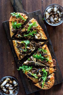 Dilimlenmiş mantar ve sığır etli pizza. Kola ile servis edilir. Koyu ahşap bir masada..