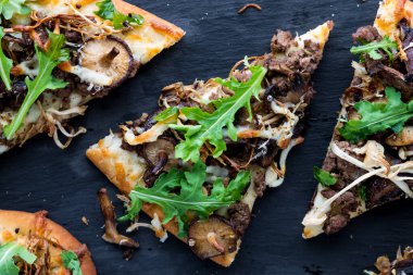 Biftek ve mantarlı ekmek dilimlerinin üstünde roka ile kaplı pizza.. 