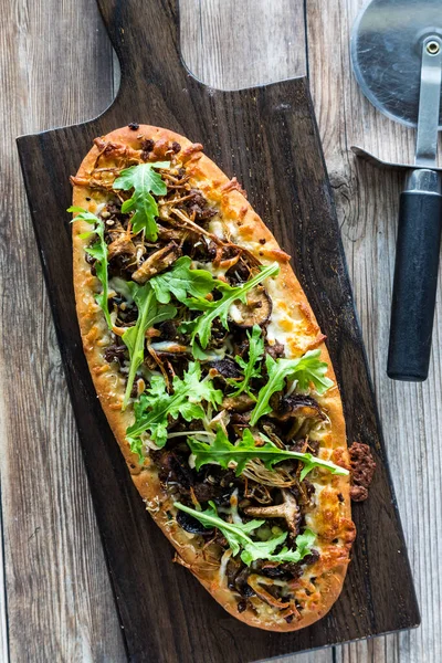 Mantar bifteği üzerine roka sürülmüş, dilimlenmeye hazır, düz ekmekli pizza..