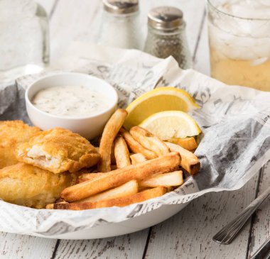 Gazete desenli parşömen kağıdında tartar sosuyla servis edilen çıtır balık ve patates kızartması.. 