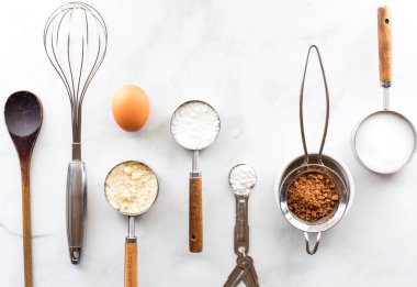 Beyaz mermer bir masa üzerinde malzemeleri olan çeşitli pişirme aletlerinin üst aşağı görünümü.