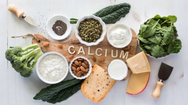 Ortasında kalsiyum sözcüğü olan ahşap bir tahtanın içinde ve çevresinde yüksek kalsiyum içeren yiyecekler..