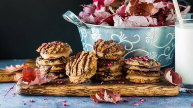 Çikolata ve karamel dantelli kurabiyeler sade bir tahtada servis edilir, kuru çiçeklerle süslenir ve sonbahar akçaağaç yapraklarıyla çevrilidir..