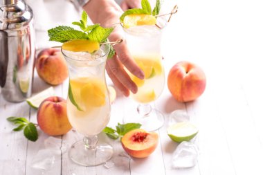 Arkasından şeftalili mojito kokteyli almak için uzanan bir el, parlak bir arka planda.