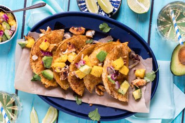 Üstünde mango avokado sosu olan bir tabak ev yapımı çıtır balık tacosu.. 