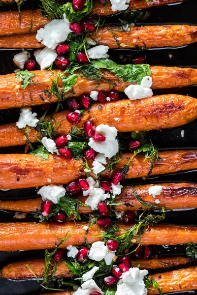 A close up of honey roasted carrots topped with goat cheese, herbs and pomegranate arils.