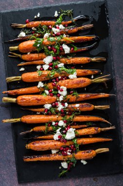 Siyah tahta üzerinde ballı havuç, keçi peyniri ve nar yağıyla kaplanmış..