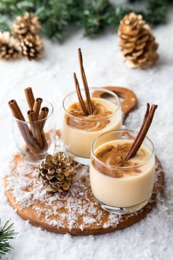 Yukarda, karla, yeşillikle ve kozalaklarla çevrili tarçınla servis edilen yumurta likörüne bakın..