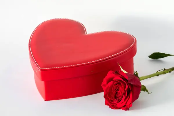 A Valentines Day leather box with a bright red rose beside against a light background.