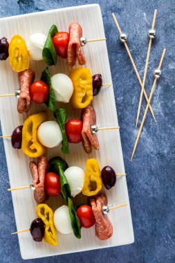 A platter of bright and colourful antipasto skewers against a blue background. 