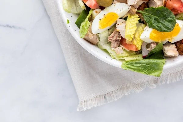 A close up of a section of a large bowl of salad with chicken and egg with copy space below.