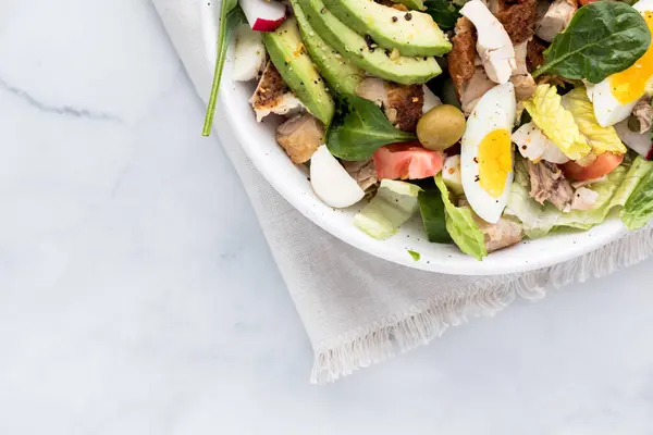 A look into a section of a large tossed salad that contains shredded chicken and sliced egg.