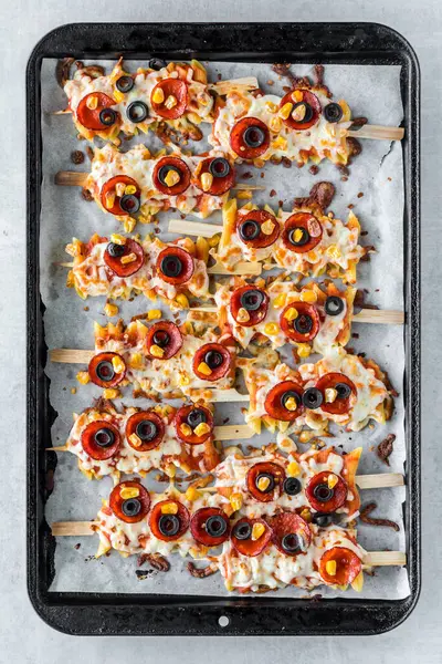 Above view of pizza pasta skewers on a parchment lined baking sheet, hot out of the oven.