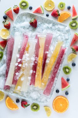 Taze meyveyle çevrili buz tepsisinin üzerinde ev yapımı dondurucu gazozların yukarıdan görünüşü. 