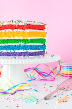 Renkli kurdeleler ve mumlarla çevrili gökkuşağı pastası..