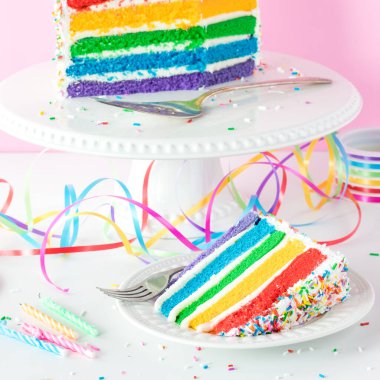 Renkli kurdeleler, serpiştirmeler ve mumlarla bir dilim gökkuşağı pastası. Kare mahsul.