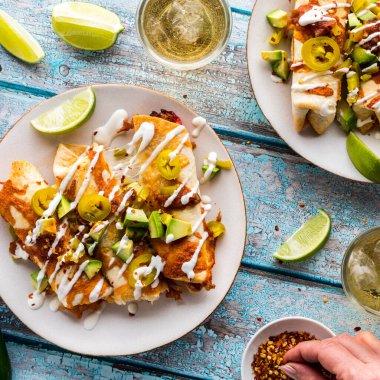 Guacamole, salsa sosu ve biberli jalapenolarla kaplı taquitos 'un tepeden aşağı manzarası..