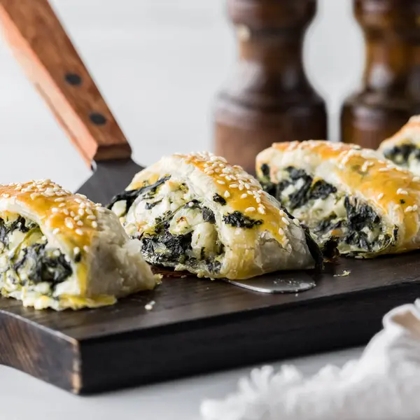 Tahta bir tahtanın üzerinde ev yapımı ıspanak ve peynirli börek servis etmeye hazır.. 