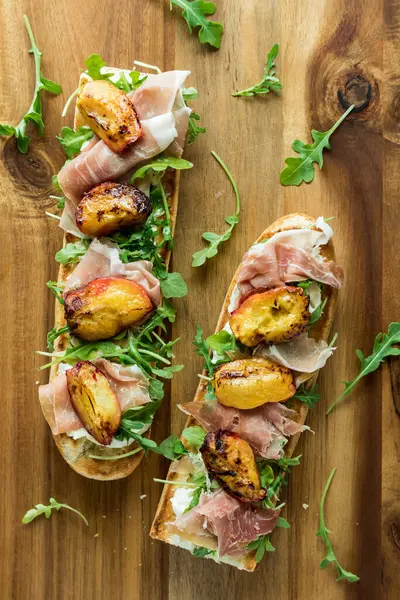 stock image A toasted peach and prosciutto baguette sandwich topped with arugula. 