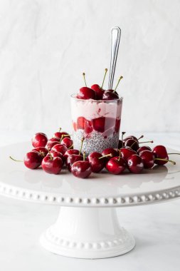 Taze kirazlarla çevrili kremalı kirazlı puding, arka planda hafif bir tezgahta..