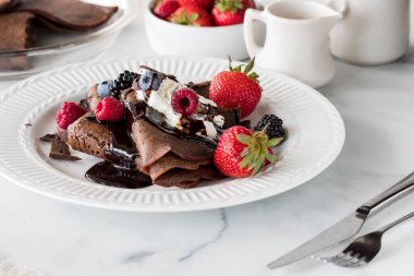 Freshly made chocolate crepes topped with whipped cream, berries and chocolate sauce. clipart