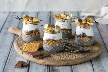 Smores chia pudingleri, ahşap bir tahtanın üzerinde, malzemelerle çevrili, yemeye hazır.. 