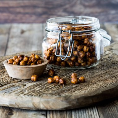 A jar and a bowl of homemade spicy roasted chick peas, on a rustic wooden board. clipart