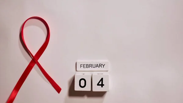 Cancer disease symbol with red ribbon on white background close-up on world Cancer Awareness Day 4 February