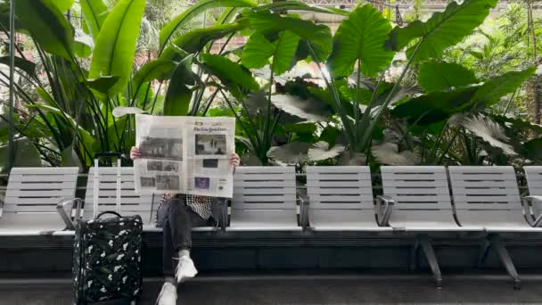 ウクライナの難民女性が待っているベンチに座って 熱帯のヤシの木がある駅のスーツケースで新聞のニューヨーク タイムズを読みます スペインマドリード — ストック動画