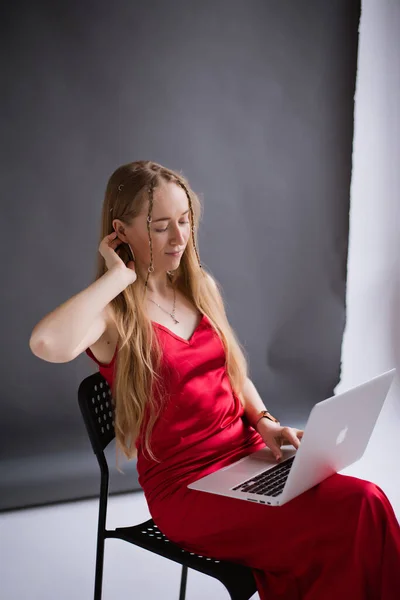 stock image A happy business woman blogger in a red dress is working, typing on a laptop apple and sitting on a chair. portrait blonde assistant of hands with computer MacBook . Vertical